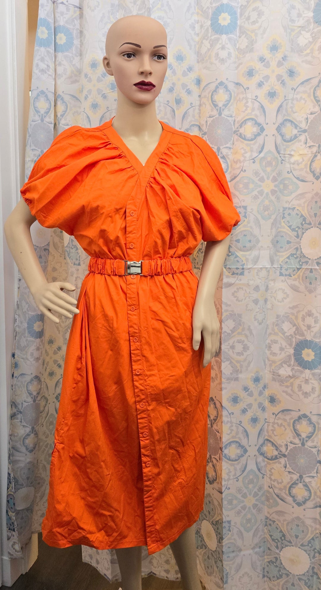 a mannequin wearing an orange dress in front of a curtain